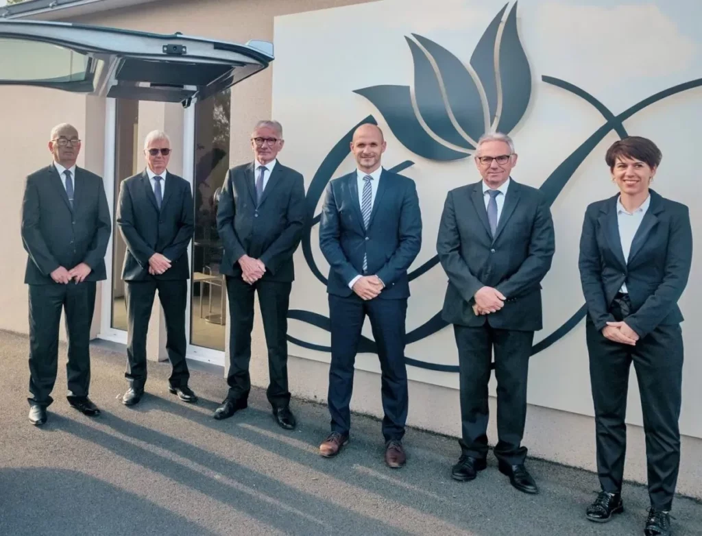 Équipe des pompes funèbres réunie devant le logo de la maison funéraire.